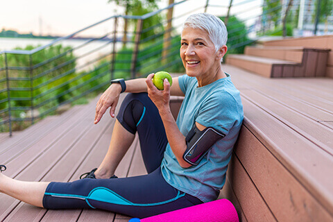 Older woman with yoga mat eating apple