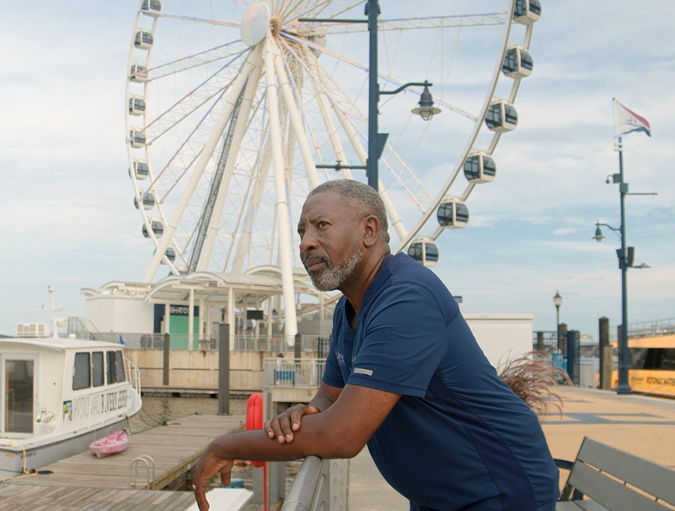 Dr. Rivers standing on a pier in front of a Ferris wheel.